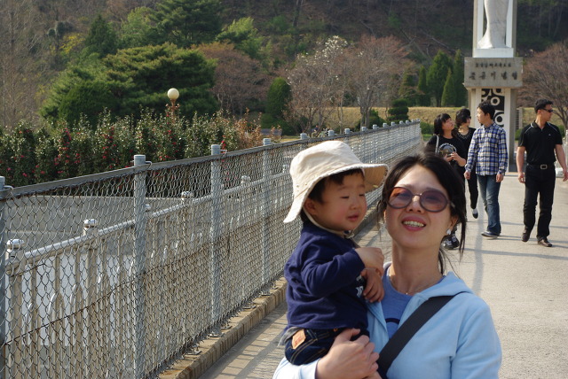 선글라스 낀 미소 띤 성인 벙거지 모자 아이 안고 울타리 옆 산책로