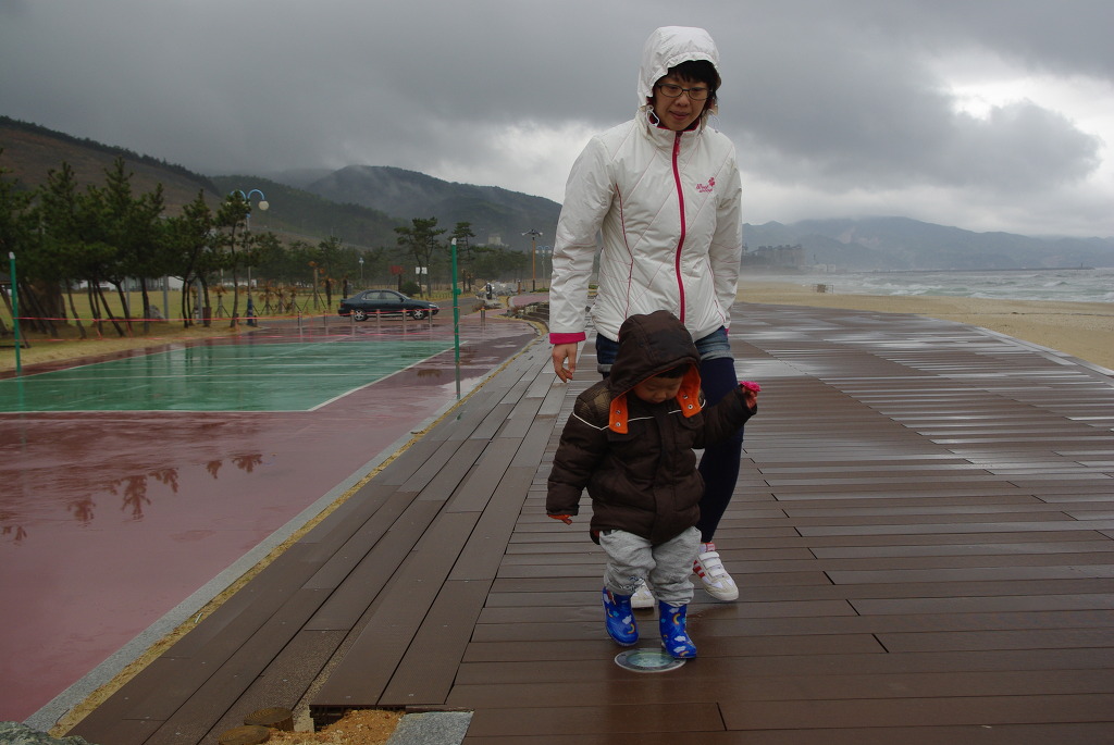 흐린 해변, 하얀 재킷 어른과 아동 젖은 산책로 걷는 중.