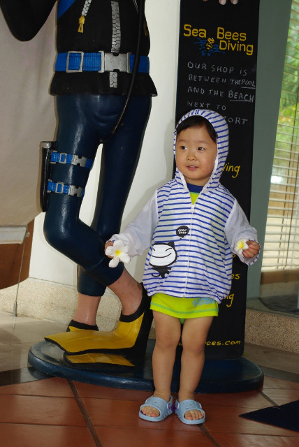 줄무늬 후드티 아동, 플루메리아 꽃 들고, 스쿠버 다이버 마네킹 옆.
