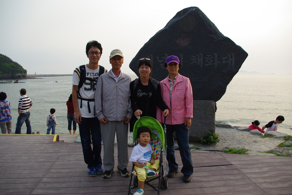 바닷가 채화대 비석 앞에서 유모차 아기와 함께한 대가족