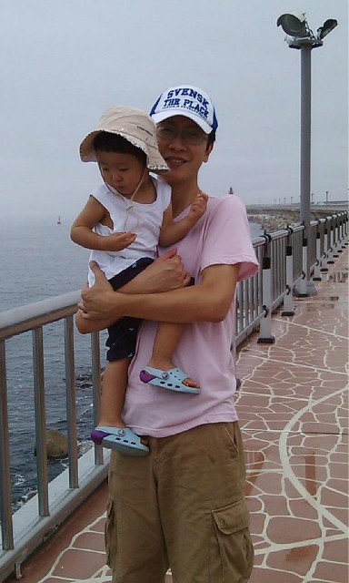 모자 쓴 미소 짓는 성인 유아 안고 해안 부두