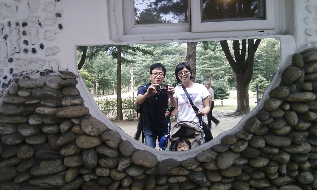 돌담 거울에 비친 부부 아기, 유모차와 숲 공원 배경